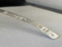 Load image into Gallery viewer, A close up on the end of the braille neckpiece. It is silver, with dots reading "and therefore powerful." The dots for the word "powerful" are accented in gold.