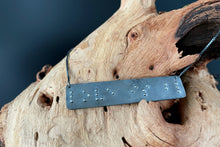 Load image into Gallery viewer, A necklace that reads "love is blind" in grade 2 braille. The piece is darkened, oxidized silver with polished silver dots, draped over a piece of driftwood.