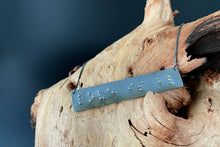 Load image into Gallery viewer, A necklace that reads "love is blind" in grade 2 braille. The piece is darkened, oxidized silver with polished silver dots, save for the word "blind", which are gold.