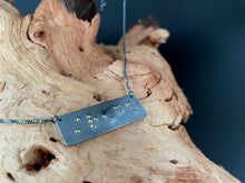 Load image into Gallery viewer, A functional, tactile braille necklace that reads "strength" in grade 2 braille. The piece is dark, oxidized silver with gold dots, draped over a piece of driftwood.