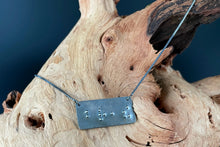 Load image into Gallery viewer, A functional, tactile braille necklace that reads "breathe" in grade 2 braille. The piece is dark, oxidized silver with polished silver dots, draped over a piece of driftwood.