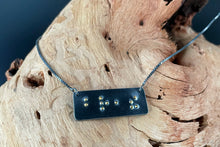 Load image into Gallery viewer, A functional, tactile braille necklace that reads "breathe" in grade 2 braille. The piece is dark, oxidized silver with gold dots, draped over a piece of driftwood.