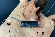 Load image into Gallery viewer, A functional, tactile braille necklace that reads "persist" in grade 2 braille. The piece is dark, oxidized silver with gold dots, draped over a piece of driftwood.