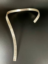 Load image into Gallery viewer, A curved silver neckpiece that wraps around the neck and then curves down the centerline of the chest. There is grade 2 braille on it, reading "It is only with the heart that one can see rightly; what is essential is invisible to the eye". The words "heart" and "essential" are done in gold.