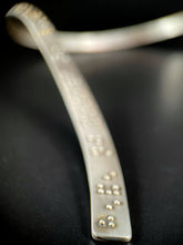 Load image into Gallery viewer, A close up of the end of this neckpiece. Only the end of the piece is in focus, and you can see the word "eye." in braille. The rest behind it fades out of focus, with only bright silver and gold dots suggesting braille bumps.