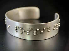 Load image into Gallery viewer, A sterling silver cuff bracelet, with accurately sized, spaced, and contracted braille. The portion that can be seen reads "in possibil".