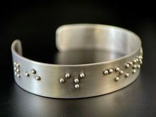 Load image into Gallery viewer, A sterling silver cuff on a black background. The cuff has accurately sized, spaced, and contracted braille. In this photo, braille reading "forever is comp" can be seen.