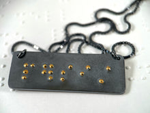 Load image into Gallery viewer, A dark, oxidized silver piece that reads "persist" in grade 2 contracted braille. The dots are done in gold.