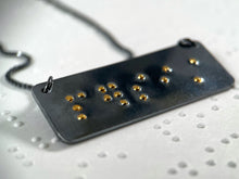 Load image into Gallery viewer, A dark, oxidized silver piece that reads "persist" in grade 2 contracted braille. The dots are done in gold.