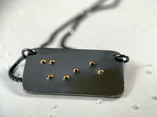 Load image into Gallery viewer, A dark, oxidized silver piece that reads "shine" in contracted grade 2 braille. The dots are done in gold.