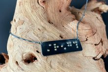Load image into Gallery viewer, A functional, tactile braille necklace that reads "strength" in grade 2 braille. The piece is dark, oxidized silver with gold dots, draped over a piece of driftwood.