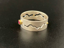 Load image into Gallery viewer, A sterling silver ring with a winding gap running down the middle of the band. There is a lab-grown round ruby in an 18k yellow gold setting in the middle of the gap, and small spacers of gold.
