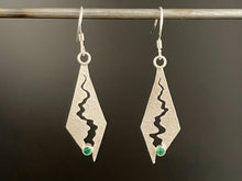 Load image into Gallery viewer, A pair of long diamond shaped sterling silver earrings. There&#39;s a long winding gap cut into the silver, which gets wider towards the bottom and culminates in a round, lab-grown emerald.
