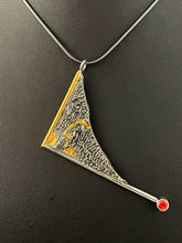 Load image into Gallery viewer, A triangular pendant hanging askew. It is framed on two sides with wire, one gold and one silver. The end of the silver frame runs off past the body of the pendant and terminates in a lab-grown orange sapphire. The body of the pendant is reticulated silver, in a rough organic texture. Rivulets of gold run through the crevices of the silver.
