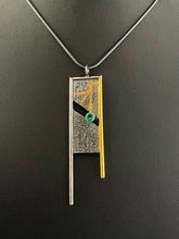 Load image into Gallery viewer, A rectangular pendant, framed on three sides with wire. The wire on the left is gold, with the top and right sides being silver. The frames hang down past the body of the pendant on the bottom. The main pendant is reticulated silver, with a rough organic texture, with traces of gold running in the crevices. It is split diagonally through the middle, with a lab grown emerald set in the gap.
