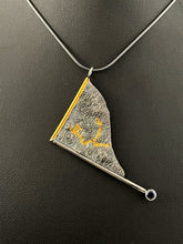 Load image into Gallery viewer, A triangular pendant, hanging askew. It is framed on two sides, one in gold covered wire, and one in silver. At the end of the framing silver wire is a lab grown blue sapphire. The body of the pendant is reticulated silver, with a rough, organic texture. Small paths of gold run along the crevices.
