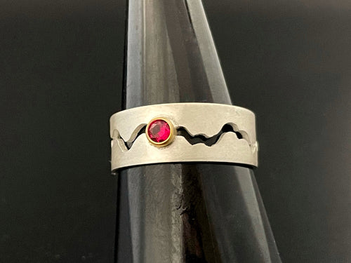 A sterling silver ring with a winding gap running down the middle of the band. There is a lab-grown round ruby in an 18k yellow gold setting in the middle of the gap.