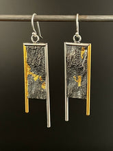 Load image into Gallery viewer, Long rectangular earrings. They are framed on the top and inside edge in silver wire, and on the outside edge in 24k gold. Each leg of the frame hangs down below the bottom of the body, with the inside silver leg longer. The body of the earring is a rough, wild texture reminiscent of land seen from air. It&#39;s oxidized and dark, with the high parts polished, and trails of gold running in the valleys of the texture.
