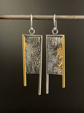 Load image into Gallery viewer, Long rectangular earrings. They are framed on the top and inside edge in silver wire, and on the outside edge in 24k gold. Each leg of the frame hangs down below the bottom of the body, with the inside silver leg longer. The body of the earring is a rough, wild texture reminiscent of land seen from air. It&#39;s oxidized and dark, with the high parts polished, and trails of gold running in the valleys of the texture.
