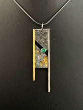 Load image into Gallery viewer, A rectangular pendant, framed on three sides with wire. The wire on the left is gold, with the top and right sides being silver. The frames hang down past the body of the pendant on the bottom. The main pendant is reticulated silver, with a rough organic texture. It is split diagonally through the middle, with a lab grown emerald set in the gap. Spots of gold shine from the crevices in the silver.
