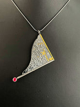 Load image into Gallery viewer, A triangular pendant, hanging askew. It is framed on two sides, one in gold covered wire, and one in silver. At the end of the framing silver wire is a lab grown ruby. The body of the pendant is reticulated silver, with a rough, organic texture. Small stripes of gold are nestled in the upper corner.
