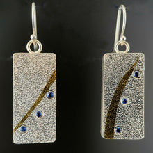 Load image into Gallery viewer, Rectangular silver earrings. This side of them is textured silver with similar but not identical gold arcs. Below the arcs there is a line of 3 lab-grown sapphires that match the flow of the gold.
