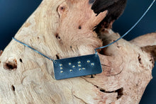 Load image into Gallery viewer, A functional, tactile braille necklace that reads &quot;love&quot; in grade 2 braille. The piece is dark, oxidized silver with gold dots, draped over a piece of driftwood.
