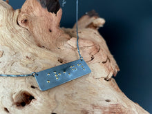 Load image into Gallery viewer, A functional, tactile braille necklace that reads &quot;strength&quot; in grade 2 braille. The piece is dark, oxidized silver with gold dots, draped over a piece of driftwood.
