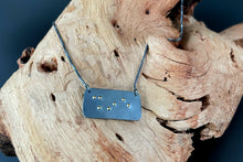 Load image into Gallery viewer, A functional, tactile braille necklace that reads &quot;shine&quot; in grade 2 braille. The piece is dark, oxidized silver with gold dots, draped over a piece of driftwood.

