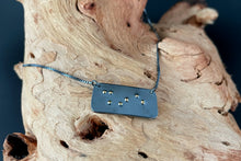Load image into Gallery viewer, A functional, tactile braille necklace that reads &quot;shine&quot; in grade 2 braille. The piece is dark, oxidized silver with gold dots, draped over a piece of driftwood.

