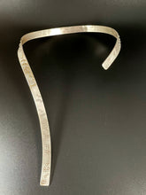 Load image into Gallery viewer, A curved silver neckpiece that wraps around the neck and then curves down the centerline of the chest. There is grade 2 braille on it, reading &quot;It is only with the heart that one can see rightly; what is essential is invisible to the eye&quot;. The words &quot;heart&quot; and &quot;essential&quot; are done in gold.
