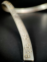 Load image into Gallery viewer, A close up of the end of this neckpiece. Only the end of the piece is in focus, and you can see the word &quot;eye.&quot; in braille. The rest behind it fades out of focus, with only bright silver and gold dots suggesting braille bumps.
