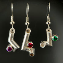 Load image into Gallery viewer, Three earrings hanging side by side. Each is made of sterling silver tubing with sharp bends making it twist and turn in three dimensions. Each has a different gemstone sitting in one of the bends - purple sapphire, ruby, and emerald.
