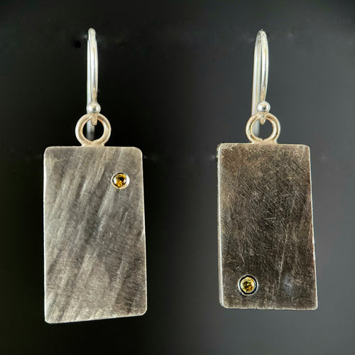Rectangular sterling silver earrings with a diagonal lined texture. Each earring has a single yellow sapphire, one in the lower left corner and the other in the upper right corner.