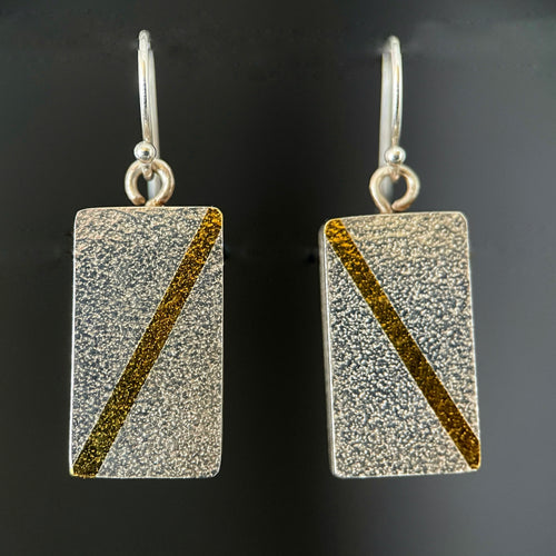 Rectangular earrings in textured silver. Each has a diagonal line of 24k gold running in opposite directions on it.