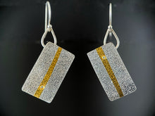Load image into Gallery viewer, These rectangular earrings hang at an angle. They are textured silver, with a line of gold running vertically down the center. In one, there is a small moissanite stone near the bottom of that gold line, and in the other it is near the top.
