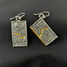 Load image into Gallery viewer, A pair of reversible earrings. These are rectangles framed in silver wire. The one on the right hangs at an angle. Within the frames is rough-textured reticulated silver. Wandering through the peaks and valleys of the texture is a bright gold path. On the tilted piece, on piece of the silver wire frame is also gold.
