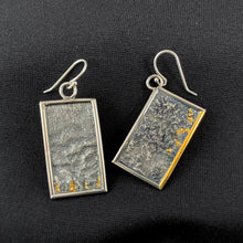 Load image into Gallery viewer, A pair of reversible earrings. These are rectangles framed in silver wire. The one on the right hangs at an angle. Within the frames is rough-textured reticulated silver. There are little flicks of gold along one edge of each piece, nestled in the valleys of the texture. On the tilted piece, on piece of the silver wire frame is also gold.
