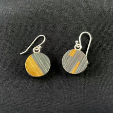 Load image into Gallery viewer, On this side the earrings are made of darkened, oxidized silver with a lined texture. The earring on the left is nearly one half gold, along a slanted line. The other has two tabs of gold reaching towards the center from the top and bottom.
