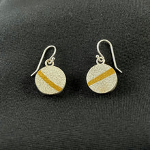 Load image into Gallery viewer, Round earrings in textured silver. There is a gold stripe across each at different angles.
