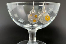Load image into Gallery viewer, This side of the round earrings are textured darkened oxidized silver. The earring on the left has 3 circles of gold in different sizes and a moissanite stone. The earring on the right has a single larger gold circle with a moissanite stone set within it.
