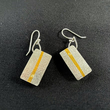 Load image into Gallery viewer, These rectangular earrings hang at an angle. They are textured silver, with a line of gold running vertically down the center. In one, there is a small moissanite stone near the bottom of that gold line, and in the other it is near the top.
