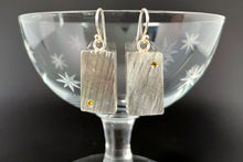 Load image into Gallery viewer, Rectangular sterling silver earrings with a diagonal lined texture hang from a small crystal glass. Each earring has a single yellow sapphire, one in the lower left corner and the other in the upper right corner.
