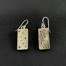 Load image into Gallery viewer, Rectangular earrings with a lined texture. The earring on the left has 3 small rubies - one in the upper and lower lefthand corners, and a third in the middle of the right side. It also has an arc of gold dots running from the upper right to lower right corners. The earring on the right has 5 scattered rubies, with bubbles of gold dots coming up from the bottom in a random pattern.
