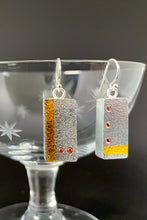 Load image into Gallery viewer, Rectangular earrings in textured silver. The earring on the left has a vertical stripe of gold near the edge, with two small orange sapphires in a horizontal line near the bottom. The earring on the right is the reverse - has a line of 3 orange sapphires arranged in a vertical line with a horizontal line in gold near the bottom.
