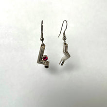 Load image into Gallery viewer, A pair of earrings. Each is made of sterling silver tubing with sharp bends in it, each earring in a different pattern. The earring on the left also has a tube-set ruby sitting in the arm of a bend.
