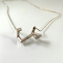 Load image into Gallery viewer, A necklace made of sterling silver tubing with sharp turns. It is vaguely U shaped, with the openings pointing out towards the viewer.
