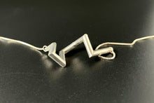 Load image into Gallery viewer, A necklace of sterling silver tubing, with sharp angles in a vague curl shape.
