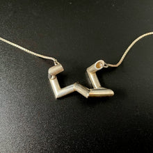 Load image into Gallery viewer, A necklace made of sterling silver tubing with sharp turns. It is vaguely U shaped, with the center of the U lifting away from the wearer.
