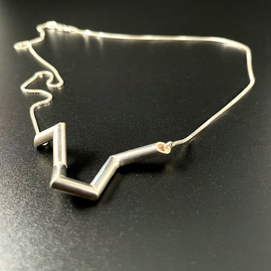 A necklace made of silver tubing, with sharp turns and twists. The overall shape is vaguely like the top of a heart.